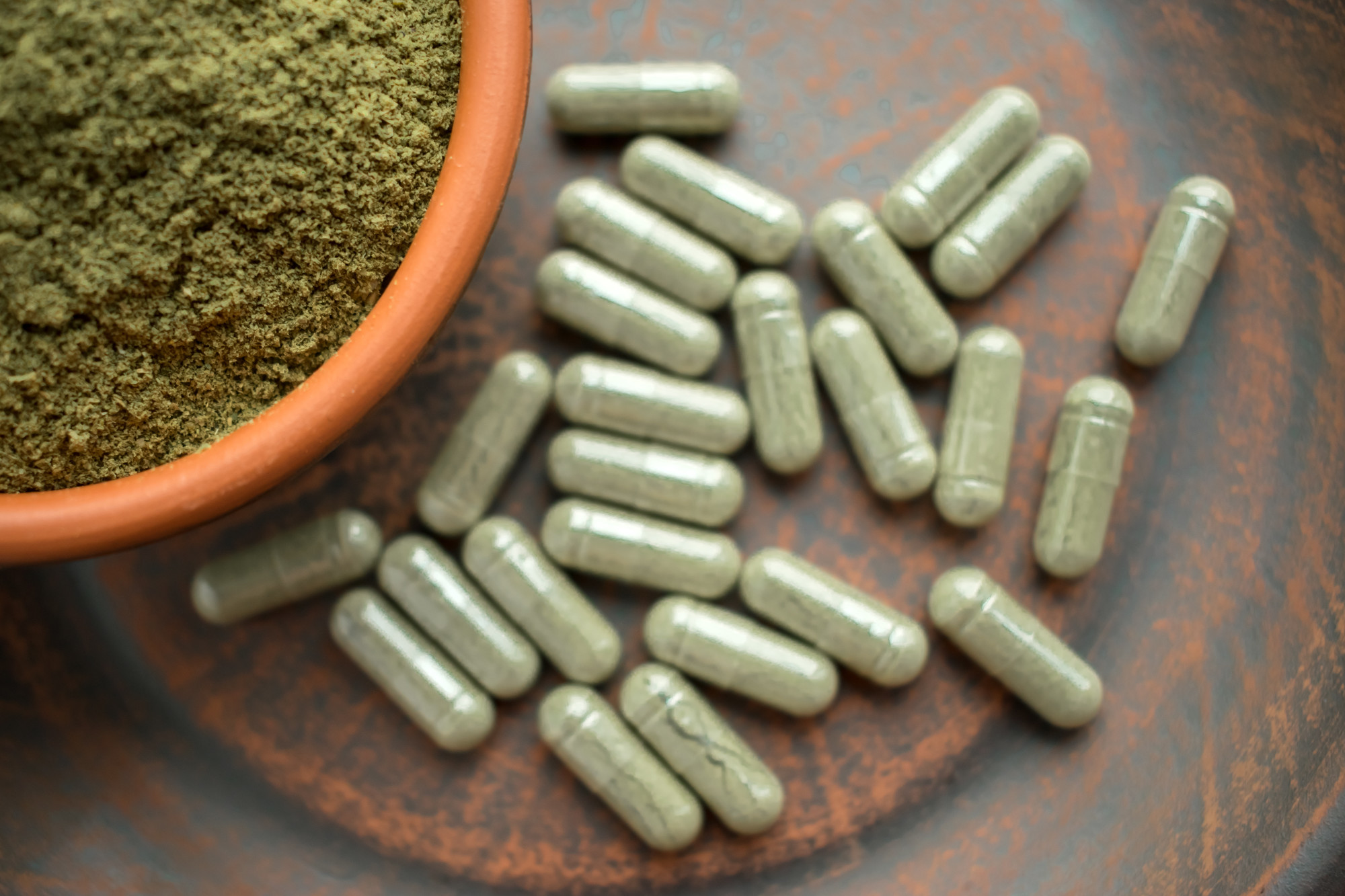 Supplement kratom green capsules and powder on brown plate. Herbal ...